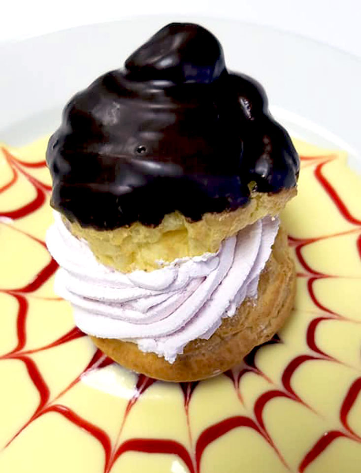 Chocolate dipped cream puff stuffed with raspberry mousse on a plate filled with creme anglaise and raspberry puree