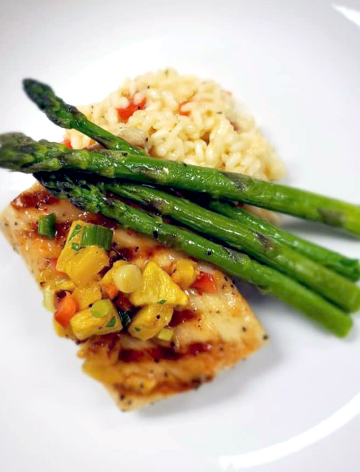 Sweet chili glazed mahi mahi beside roasted red pepper & smoked gouda risotto with asparagus with herb citrus butter place diagonally on top all on a plate
